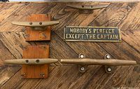 Four brass boat cleats (two on wood blocks, two loose) and brass captain sign displayed on wood surface