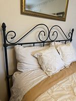 Front view of black wrought iron headboard attached to queen bed, shows scrollwork and finials