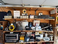 Wide view of top and middle shelves showing networking devices, radios, speakers, cameras and accessories