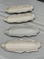 Four white ceramic corn-shaped dishes arranged in row