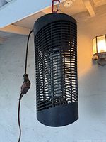 Full view of cylindrical black bug zapper suspended from ceiling showing grill, UV tube and power cord