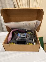 Opened box showing assembled four-wheel robot, electronics and bagged parts