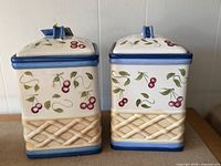 Front view of both ceramic cherry canisters showing design and lids