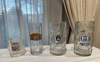 Four beer glasses lined up left to right showing size comparison and logos