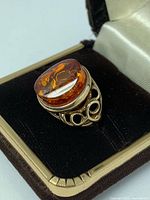 Ring in presentation box showing amber cabochon and scrollwork band