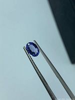 Oval tanzanite held in tweezers showing violet-blue hue
