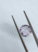 Oval lavender gemstone held by tweezers, top facet view