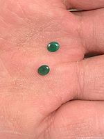 Pair of emeralds on fingertip showing size and oval shape