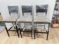 Front view of three matching bar chairs wrapped in plastic