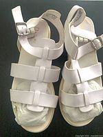 Top view of white strappy sandals with stuffing, Daphne logo visible