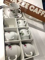 Box with six porcelain espresso cups and stacked saucers visible
