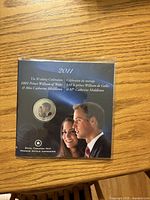 Front view of sealed presentation sleeve displaying colour portrait coin and images of Prince William and Catherine