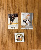 Fronts of two Bobby Orr trading cards and coin