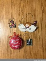 All four teacher-themed Christmas ornaments on wood surface