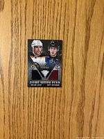 Front of dual jersey card showing player images, team logos, and two fabric swatches