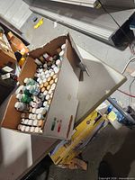 Top view of cardboard box showing numerous acrylic paint bottles of various colors and sizes