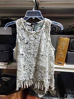 Front view of white crochet lace sleeveless top with fringe hem