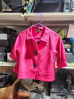 Front view of pink cropped jacket on hanger showing three black buttons and half sleeves