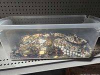 Overview of clear plastic bin filled with mixed costume jewelry pieces