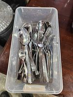 Top view of plastic bin showing mix of stainless steel forks and spoons