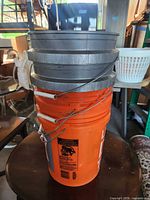Four stacked 5-gallon buckets, two orange Home Depot, two gray Lowe’s, showing exterior and handles