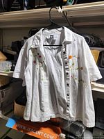 Front view of white short-sleeve beaded button-up shirt on hanger
