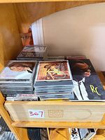 Stack of CD cases on wooden shelf, assorted artists visible