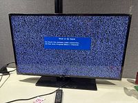 Front view of Samsung TV powered on displaying no-signal screen with remote and power cable visible