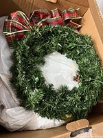Top view of green artificial wreath with red-green plaid bow and pinecone, showing PVC needles and wiring