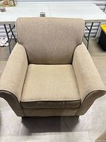 Front view of beige upholstered armchair with flared arms and tapered legs