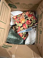 Box with assorted linens showing pumpkin placemats, green towel, lace edge cloth