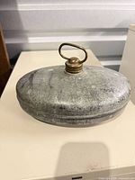 Side view of galvanized hot water bottle showing loop handle on brass cap