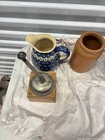 Coffee grinder, blue folk pitcher and stoneware crock on packing paper