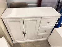 Front view of white storage cabinet showing three drawers and two doors