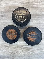 Front view showing logos of three vintage Cooper Official pucks—one gold, two orange—displaying wear