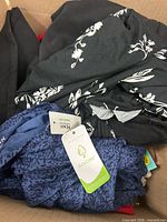 View into box showing black floral piece and blue patterned piece with tags