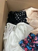 Box top view showing white satin garment with label, black polka dot piece and floral fabric