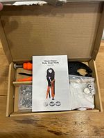 Open box showing pliers, instruction sheet, snap components and accessories