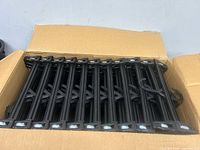 Open box filled with stacked black plastic pant hangers