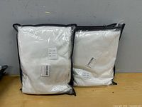 Two sealed white bedding sets on table