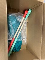 View of open box showing teal polka-dot fabric and two wooden-handle cleaning tools