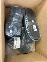 Box containing two wrapped black slide sandals and additional wrapped item