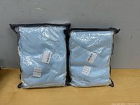 Two sealed light blue bedding sets in plastic packaging on table
