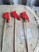 Three red bird figures on sticks laid out on surface