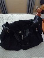 Full view of black duffle bag on bed showing size and handles