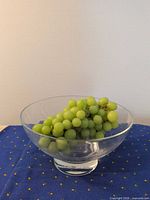 Clear glass footed bowl on blue cloth with grapes placed inside