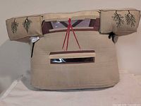 Front view showing tan buckskin pillow with embroidery, vinyl windows and red ribbons