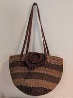 Full view of handwoven striped sisal tote with leather straps hanging on wall