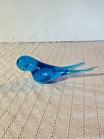Side view of cobalt/aqua glass bird figurine on fabric surface