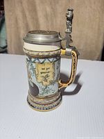 Full view of stein showing lid, handle, banner text and relief decoration